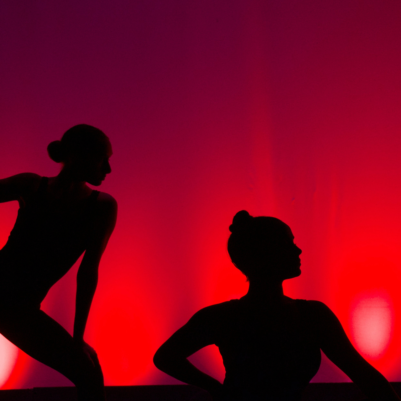 Photo of a silhouette of 2 dancers posing in front of a red curtain.